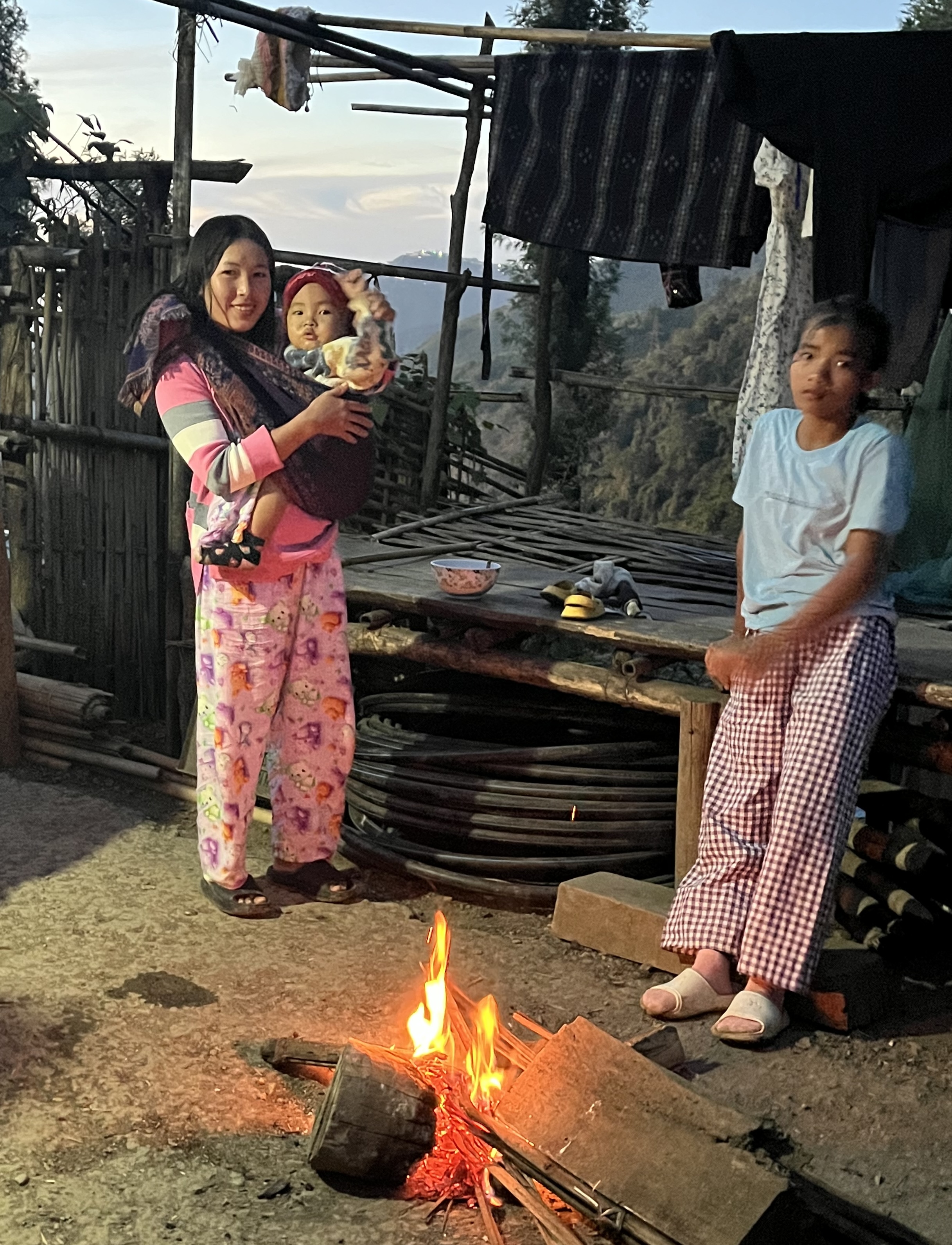 Family gathered around a campfire outside their shelter, Mizoram