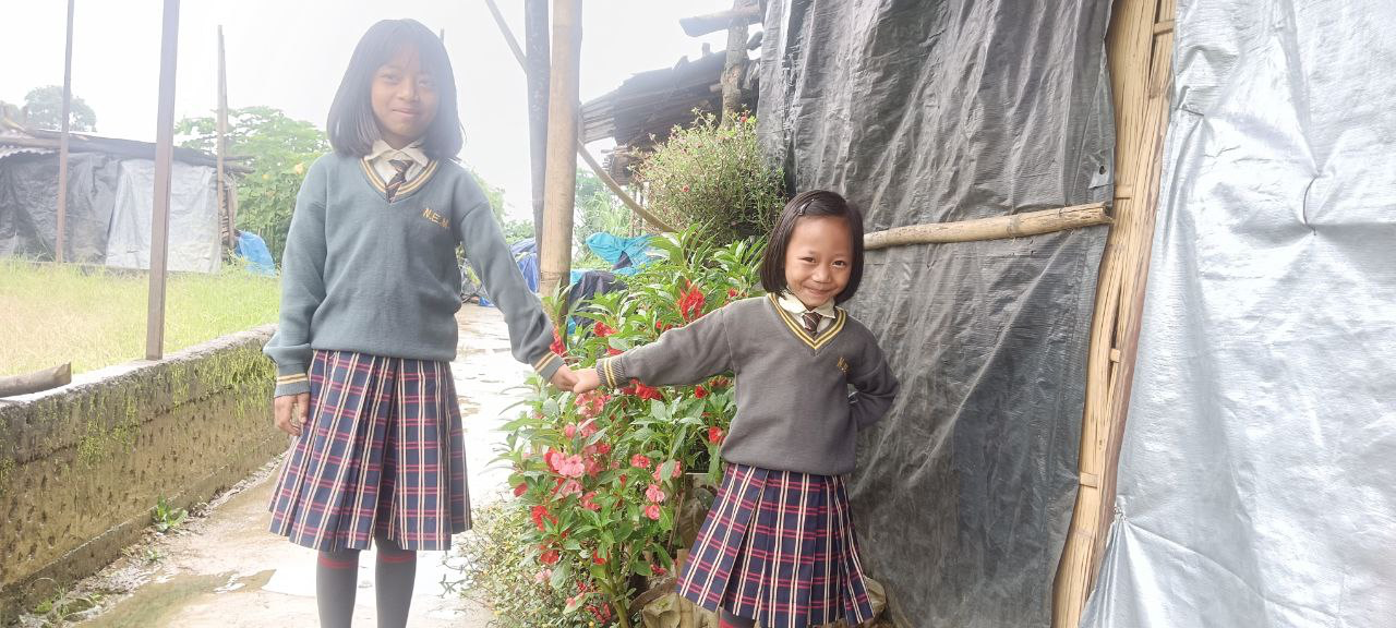 Two girls in school uniforms outside a camp shelter, Mizoram